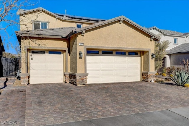 traditional home featuring solar panels, stucco siding, a garage, stone siding, and decorative driveway