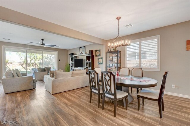 dining area with ceiling fan with notable chandelier, hardwood / wood-style floors, and plenty of natural light