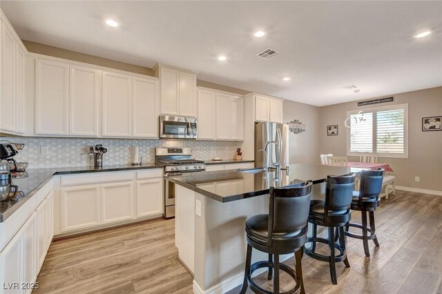 kitchen featuring stainless steel appliances, sink, white cabinetry, light hardwood / wood-style floors, and a kitchen island with sink