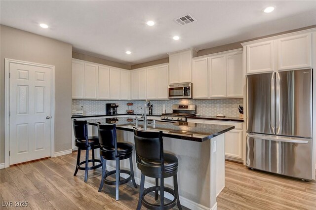 kitchen featuring appliances with stainless steel finishes, light hardwood / wood-style flooring, a kitchen island with sink, and white cabinetry