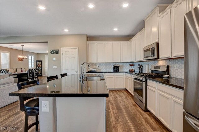 kitchen with stainless steel appliances, sink, white cabinets, a center island with sink, and pendant lighting