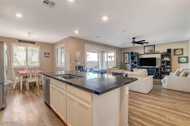 kitchen with an island with sink, light hardwood / wood-style floors, appliances with stainless steel finishes, dark stone countertops, and sink