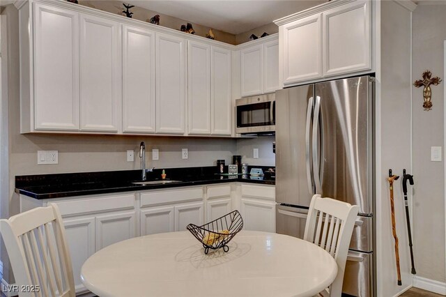 kitchen with stainless steel appliances, white cabinetry, dark stone countertops, and sink