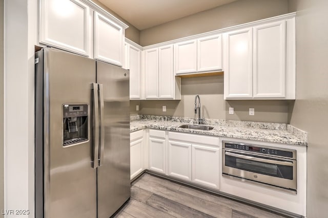 kitchen with sink, stainless steel appliances, light wood-type flooring, and white cabinetry