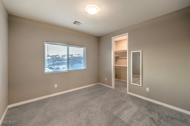 unfurnished bedroom featuring a walk in closet, a closet, and light carpet