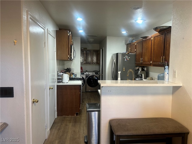 kitchen featuring a breakfast bar area, appliances with stainless steel finishes, washer and dryer, kitchen peninsula, and dark wood-type flooring