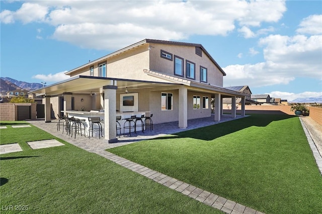 rear view of property featuring an outdoor bar, a lawn, and a patio