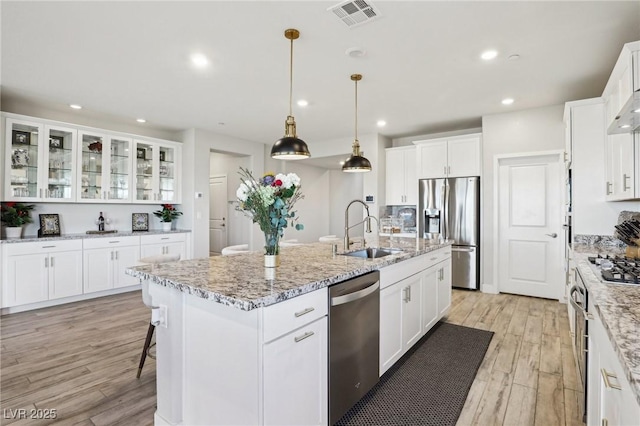 kitchen with appliances with stainless steel finishes, sink, white cabinetry, a kitchen island with sink, and light hardwood / wood-style floors