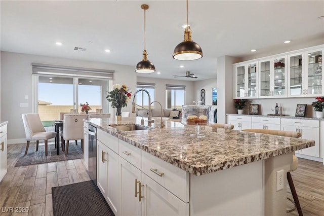 kitchen with light stone countertops, white cabinetry, a kitchen island with sink, sink, and decorative light fixtures