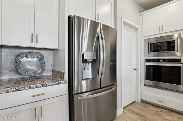 kitchen with light hardwood / wood-style flooring, white cabinetry, dark stone countertops, decorative backsplash, and stainless steel appliances