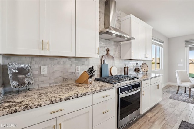 kitchen with wall chimney exhaust hood, white cabinets, decorative backsplash, and appliances with stainless steel finishes