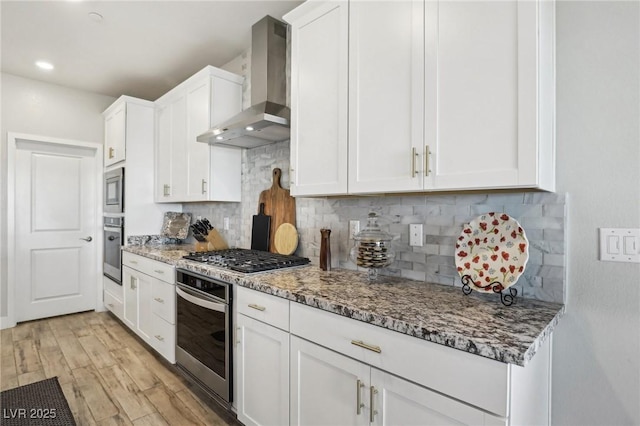 kitchen featuring white cabinetry, stone counters, wall chimney range hood, and appliances with stainless steel finishes