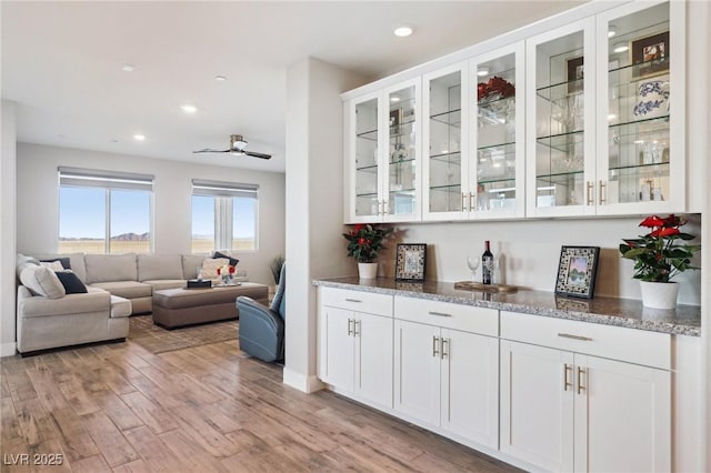 bar with ceiling fan, white cabinetry, light hardwood / wood-style floors, and stone countertops