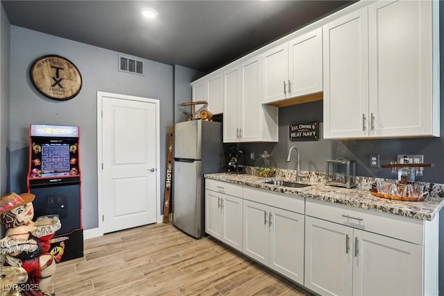 kitchen featuring sink, white cabinetry, stainless steel refrigerator, and light stone counters