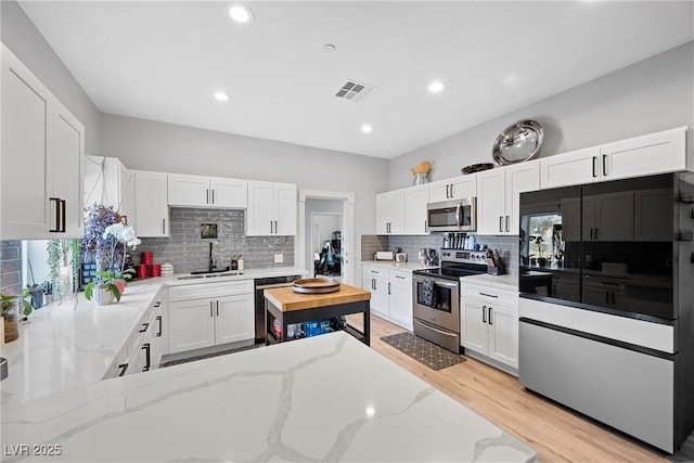 kitchen with stainless steel appliances, sink, white cabinets, light hardwood / wood-style floors, and light stone countertops