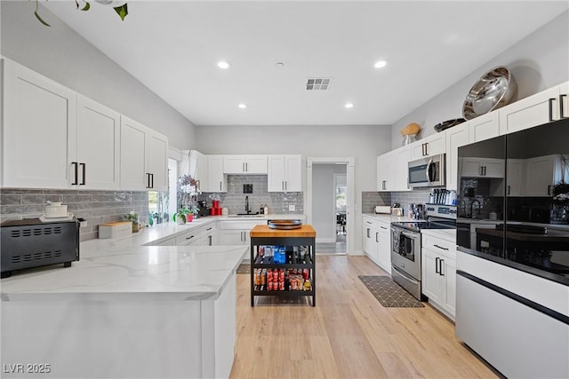 kitchen with sink, stainless steel appliances, white cabinetry, and light stone counters