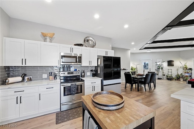 kitchen with stainless steel appliances, white cabinetry, light stone counters, and tasteful backsplash