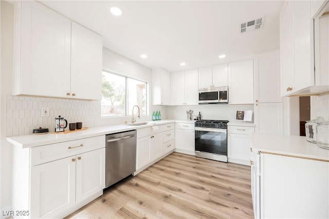 kitchen featuring light hardwood / wood-style floors, stainless steel appliances, sink, white cabinetry, and backsplash