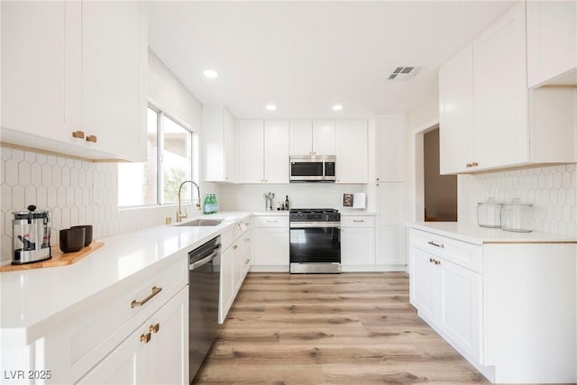 kitchen with backsplash, stainless steel appliances, white cabinets, and sink