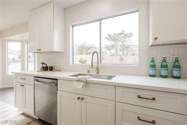 kitchen featuring white cabinets, light hardwood / wood-style floors, decorative backsplash, sink, and stainless steel dishwasher