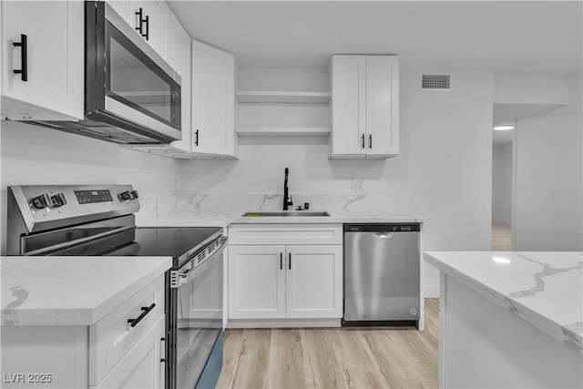 kitchen with light stone counters, stainless steel appliances, light wood-type flooring, white cabinetry, and sink