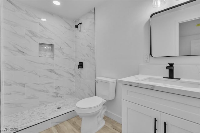 bathroom featuring tiled shower, hardwood / wood-style floors, vanity, and toilet