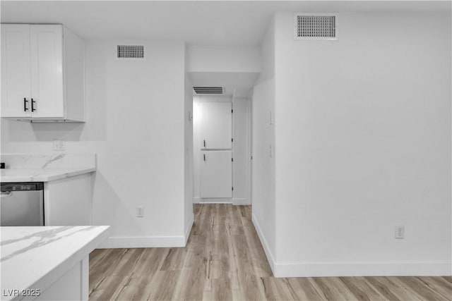 kitchen with light hardwood / wood-style flooring, white cabinetry, stainless steel dishwasher, and light stone countertops