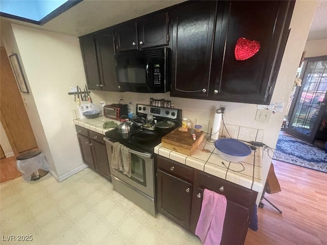 kitchen featuring a skylight, tile countertops, and stainless steel range with electric stovetop