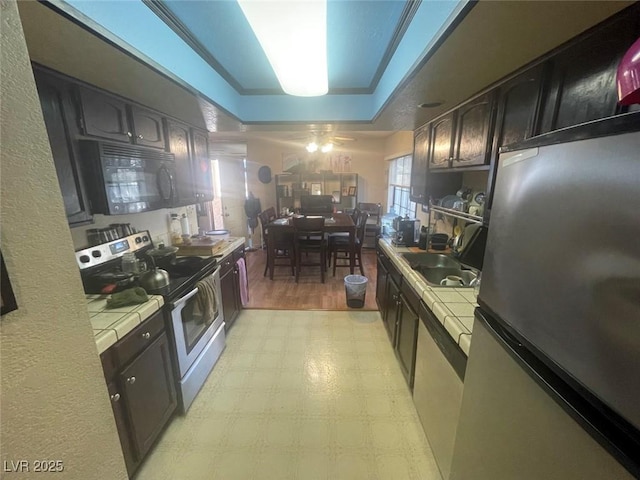 kitchen with stainless steel appliances, dark brown cabinetry, tile countertops, and sink