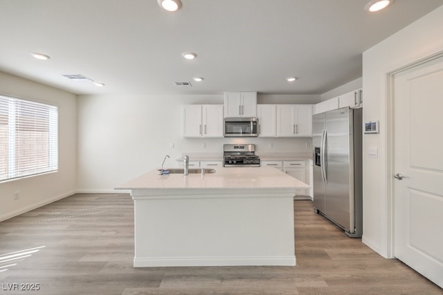 kitchen with sink, white cabinetry, light hardwood / wood-style floors, an island with sink, and appliances with stainless steel finishes