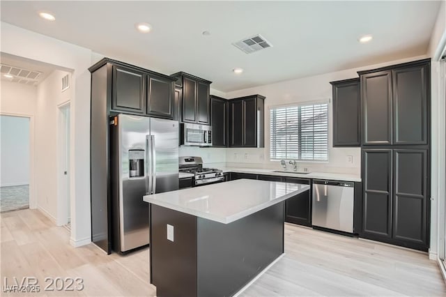 kitchen featuring appliances with stainless steel finishes, light wood-type flooring, a center island, and sink