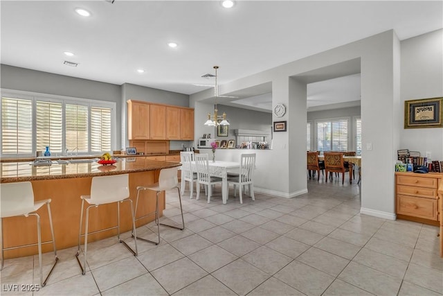 kitchen featuring light stone counters, pendant lighting, light brown cabinetry, light tile patterned floors, and a kitchen breakfast bar