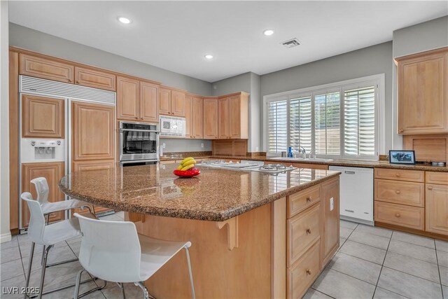 kitchen featuring a kitchen breakfast bar, a center island, stone counters, built in appliances, and sink