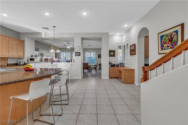 kitchen featuring dark stone countertops, light tile patterned floors, ceiling fan, a breakfast bar area, and pendant lighting