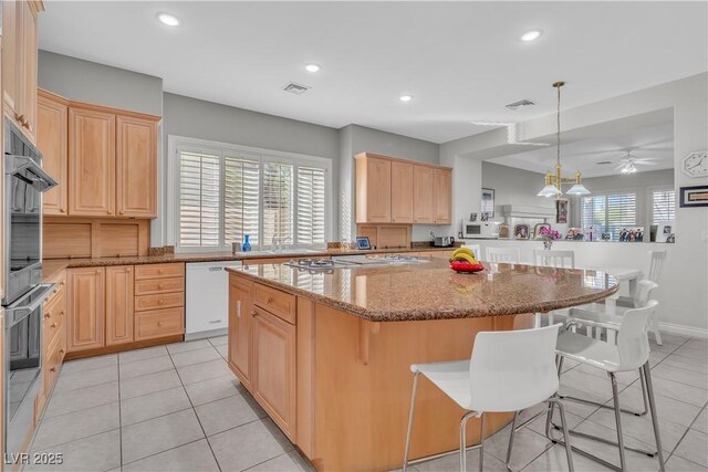 kitchen featuring white appliances, a kitchen bar, light brown cabinetry, and kitchen peninsula