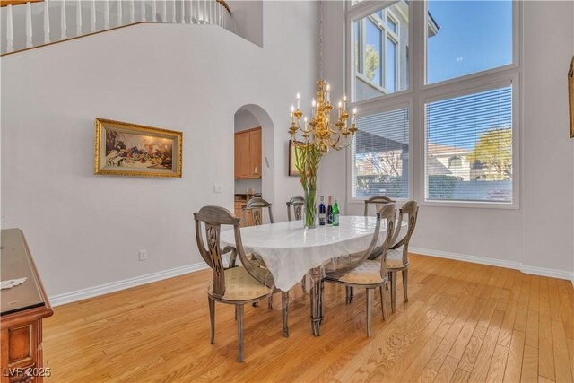 dining space featuring a notable chandelier, light wood-type flooring, and a towering ceiling