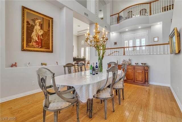 dining space with a towering ceiling, light wood-type flooring, and a chandelier