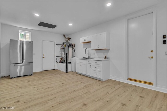 kitchen featuring white cabinets, stainless steel fridge, light wood-type flooring, and sink