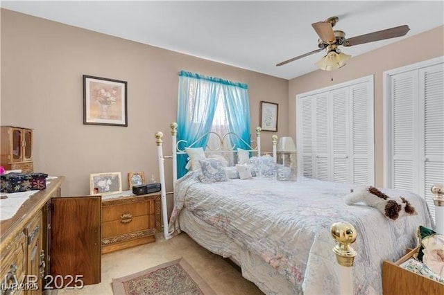 bedroom with ceiling fan, two closets, and light carpet