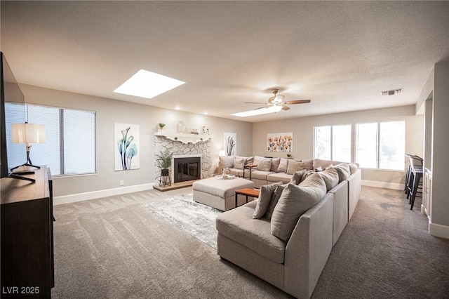 carpeted living room featuring a fireplace, ceiling fan, and a skylight