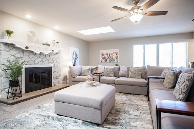 carpeted living room featuring a skylight, a fireplace, and ceiling fan