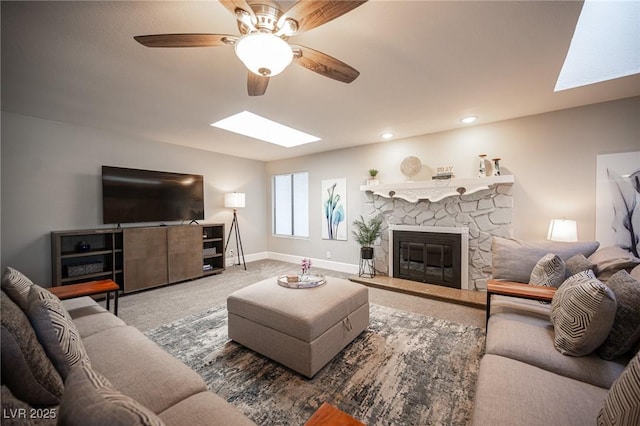 living room featuring ceiling fan, a skylight, carpet flooring, and a fireplace