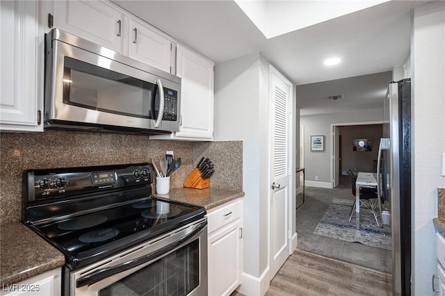 kitchen featuring white cabinets, dark stone countertops, light wood-type flooring, decorative backsplash, and appliances with stainless steel finishes