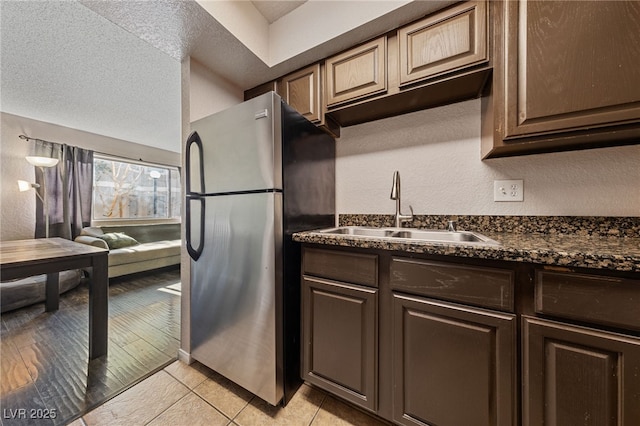 kitchen with a textured ceiling, stainless steel fridge, light tile patterned floors, dark stone counters, and sink