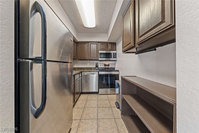 kitchen with stainless steel appliances, a raised ceiling, light tile patterned floors, and dark brown cabinetry