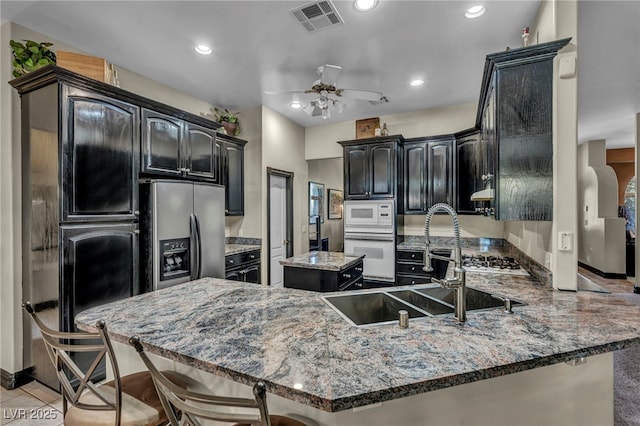 kitchen featuring sink, white appliances, ceiling fan, kitchen peninsula, and dark stone counters