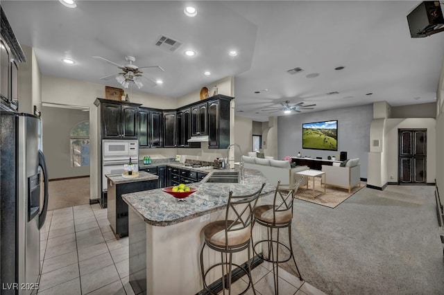 kitchen featuring light carpet, white microwave, light stone counters, stainless steel refrigerator with ice dispenser, and sink