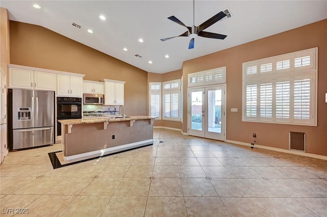 kitchen with stainless steel appliances, french doors, tasteful backsplash, light stone countertops, and a center island with sink