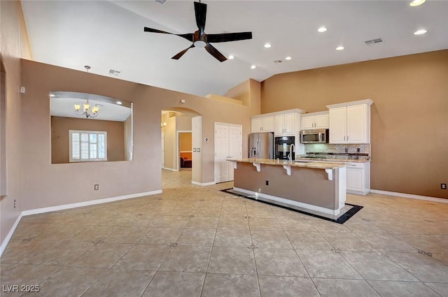 kitchen featuring light stone counters, an island with sink, a kitchen bar, ceiling fan with notable chandelier, and appliances with stainless steel finishes