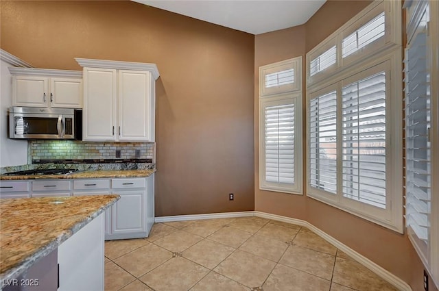 kitchen featuring stainless steel appliances, light stone countertops, light tile patterned floors, white cabinets, and tasteful backsplash